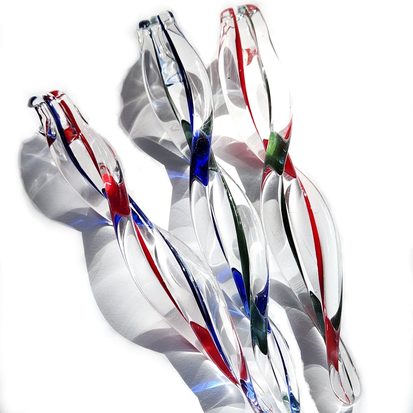 Trio of twisted glass icicle ornaments with colorful swirls casting shadows. Elegant seasonal decor for Christmas trees or windows.