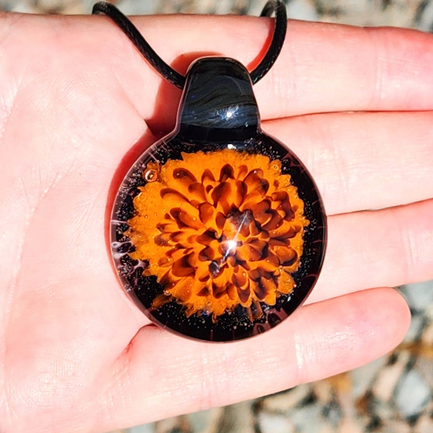 Fiery Glass Pendant Necklace held in hand, showing scale and detail of orange and red bloom. Handmade Halloween-inspired blown glass jewelry.