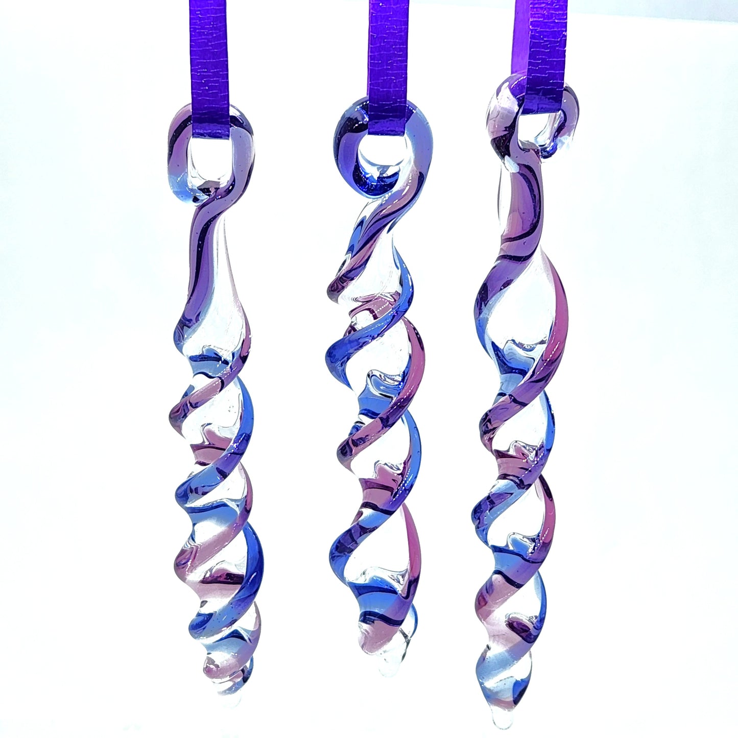Trio of handmade blue and purple glass icicle ornaments hanging on purple ribbons, perfect as suncatchers or holiday decorations.