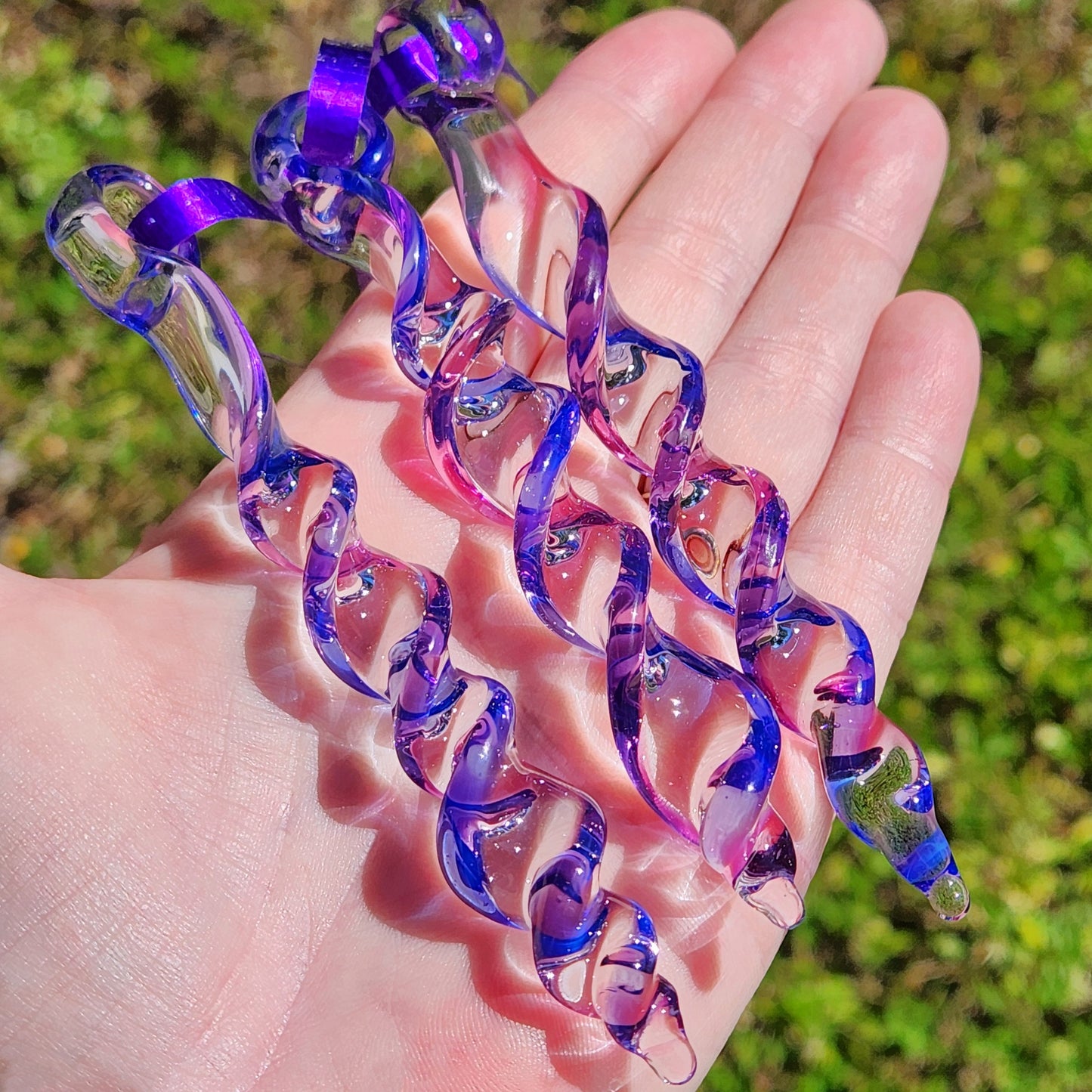 Hand holding 3 handmade blue and purple glass icicle ornaments, showcasing their intricate spiral design and vibrant colors in sunlight.