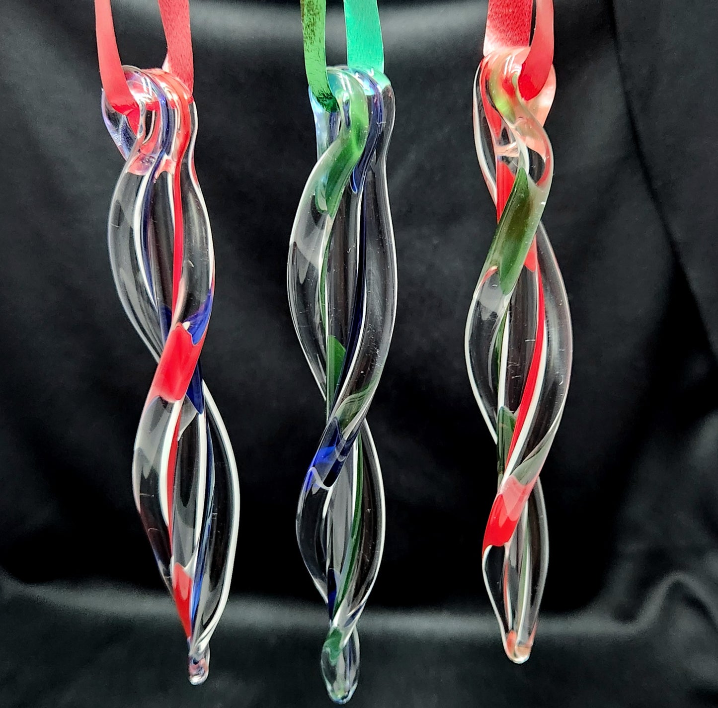 Three hanging handmade glass ornaments with red, green, and blue ribbons. Twisted icicle design adds sparkle to holiday decor.