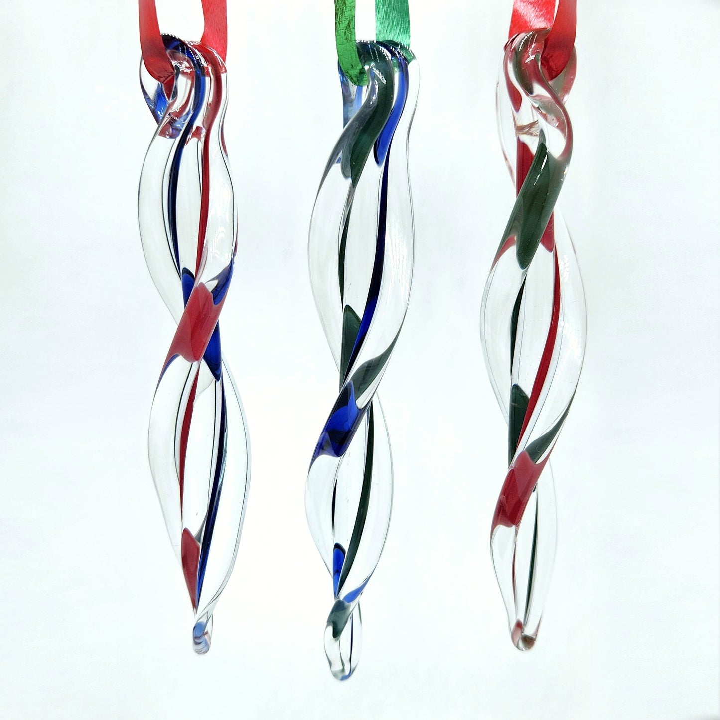 Handblown glass icicle ornaments suspended on red and green ribbons. Each ornament features a unique swirl pattern for festive charm.