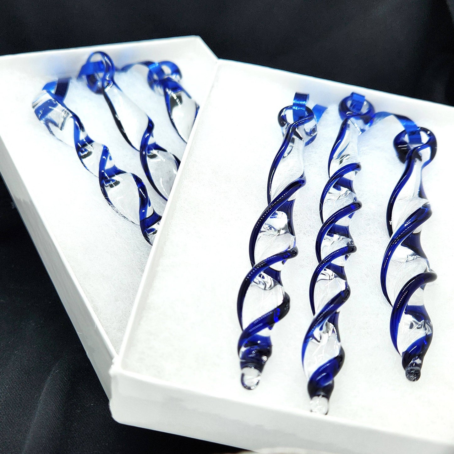 Two white boxes of handmade blue glass Christmas ornaments. Twisted icicle suncatchers crafted for festive home and garden decoration.