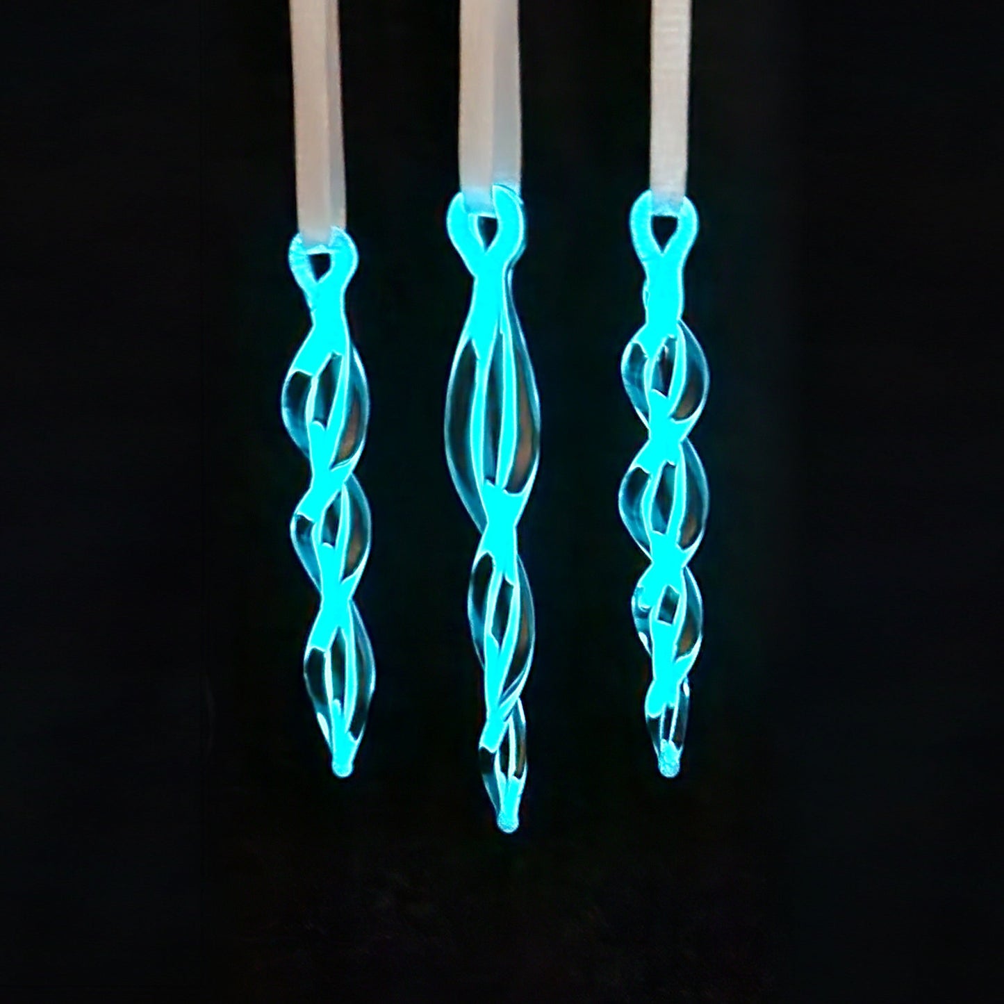 Glow-in-the-dark Christmas tree glass ornaments shaped like twisted icicles with blue luminescence. Unique holiday decor for seasonal tree accents.