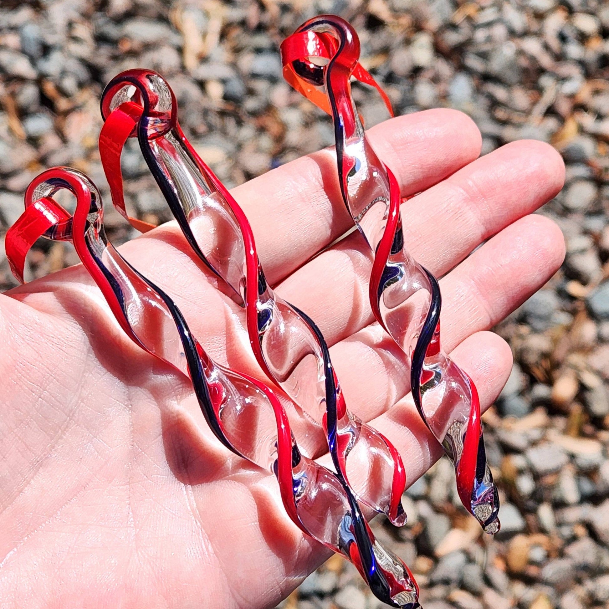 Close-up of Red & Blue Glass Christmas Ornaments held in hand, highlighting the intricate handmade icicle twist and vibrant holiday colors.
