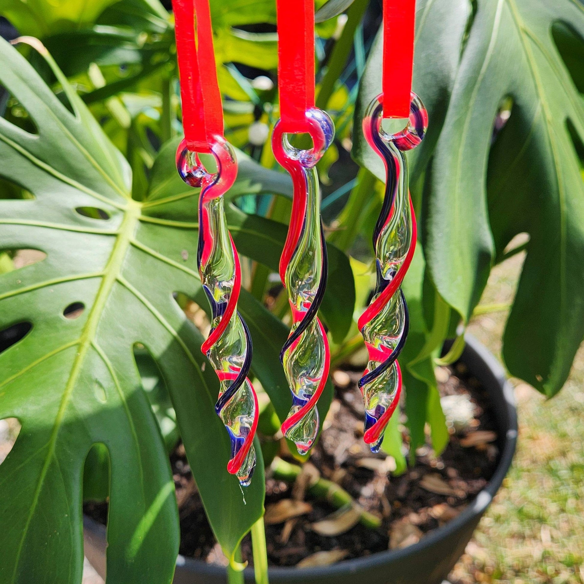 Red & Blue Glass Christmas Ornaments hanging outdoors with tropical leaves in background, highlighting their handmade twisted icicle design.