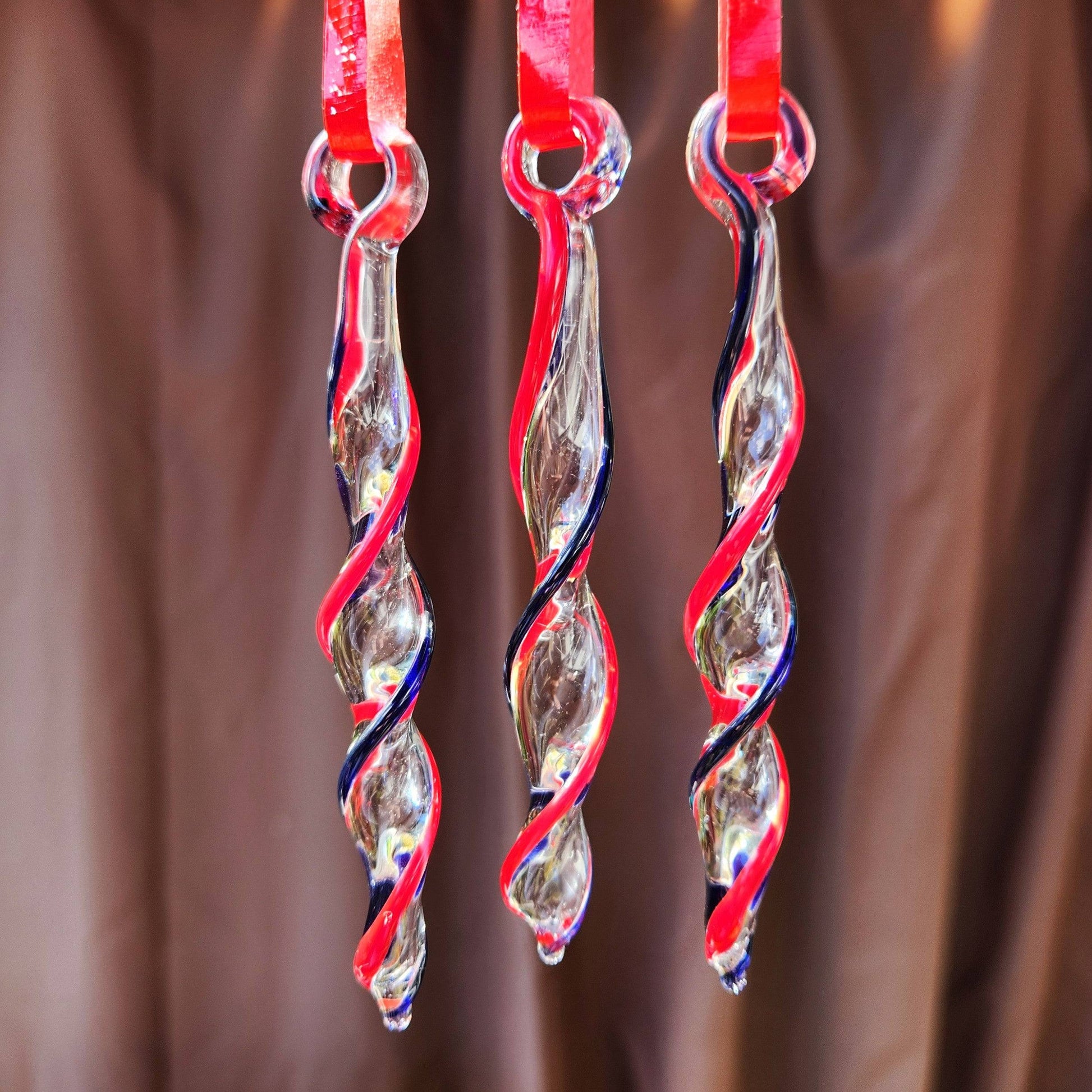 Three Red & Blue Glass Christmas Ornaments hanging against a brown background, showcasing their elegant handmade icicle twist design.