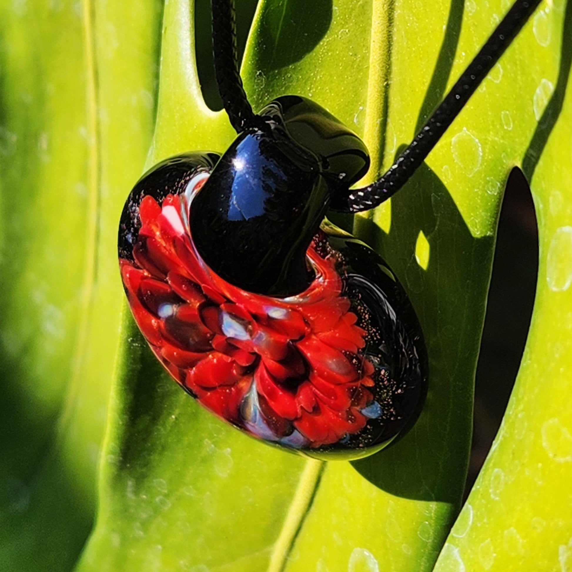 Handmade blown glass pendant with red flower encased in black glass, suspended on a cord. Unique borosilicate jewelry design gift for any occasion.