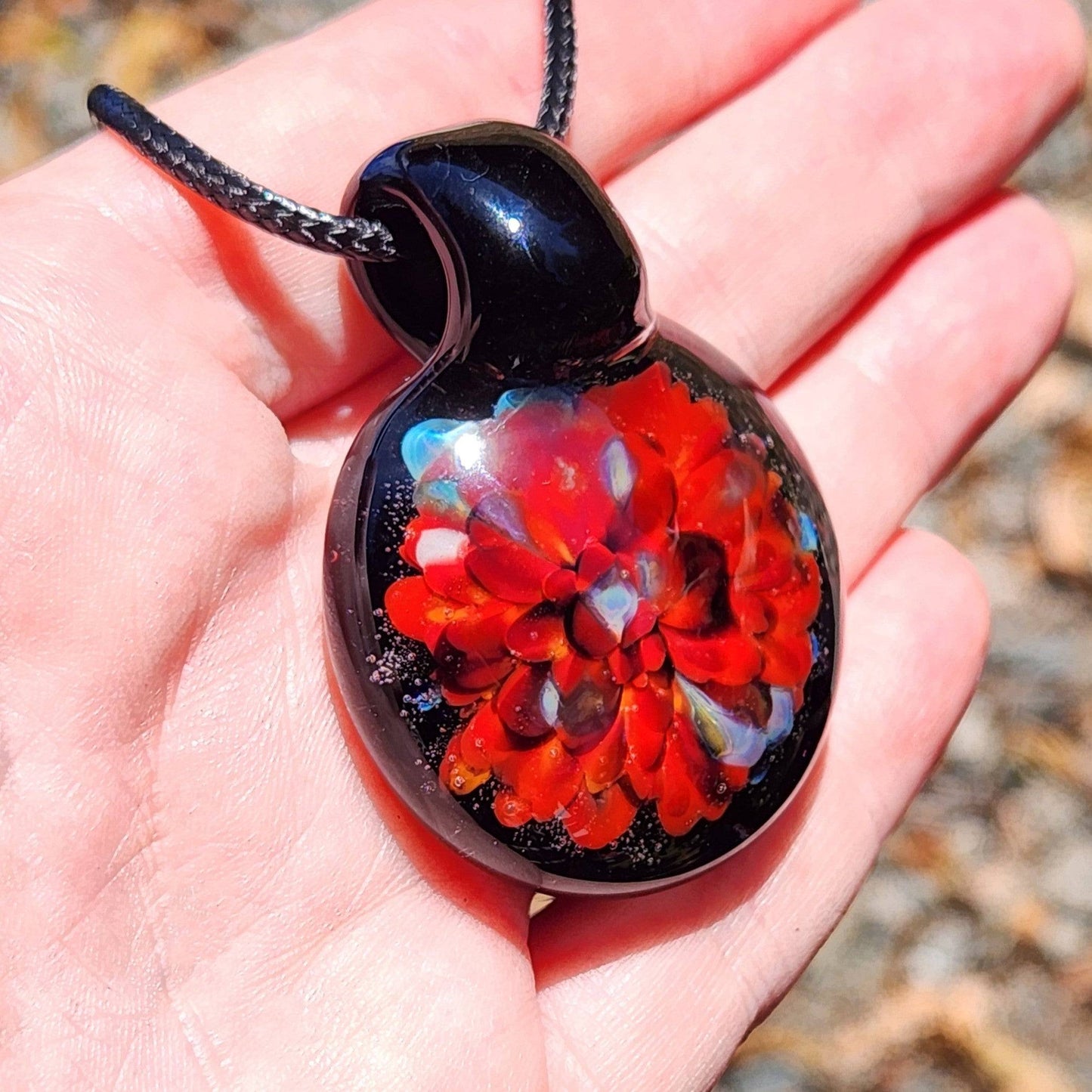Hand holding radiant red glass pendant necklace with multicolor highlights. Unique handmade borosilicate pendant perfect for gifting.