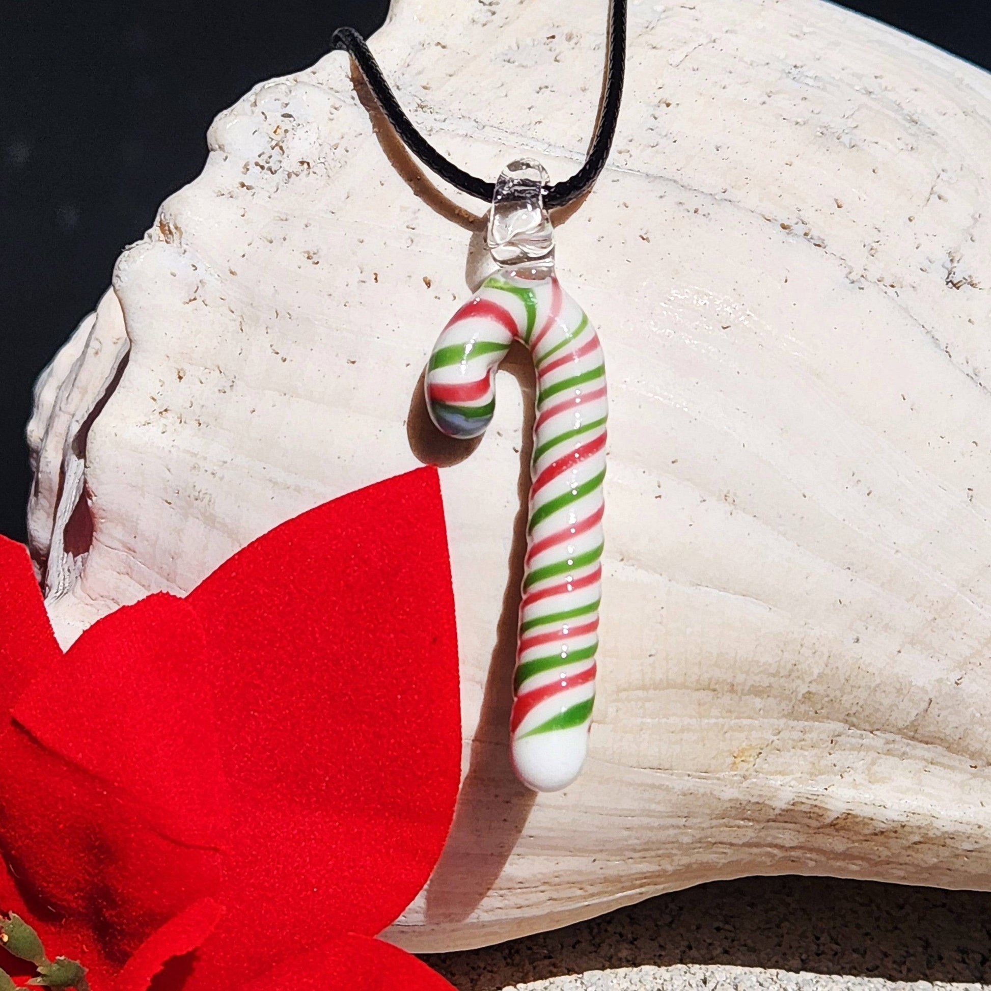 Handmade glass candy cane pendant necklace hanging on a shell with red bow, showcasing its festive red, green, and white swirl design.