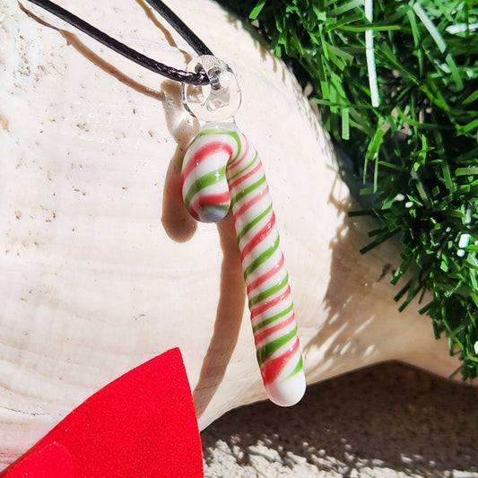 Handmade glass candy cane pendant necklace with red, green, and white swirls, perfect for Christmas jewelry gift. Displayed on a seashell with festive decor.