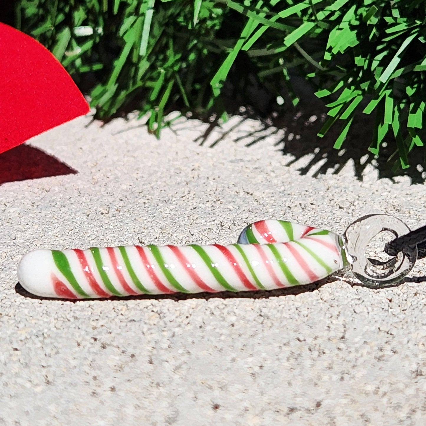 Side view of handmade glass candy cane pendant necklace lying flat, featuring red, green, and white holiday stripes for a festive look.