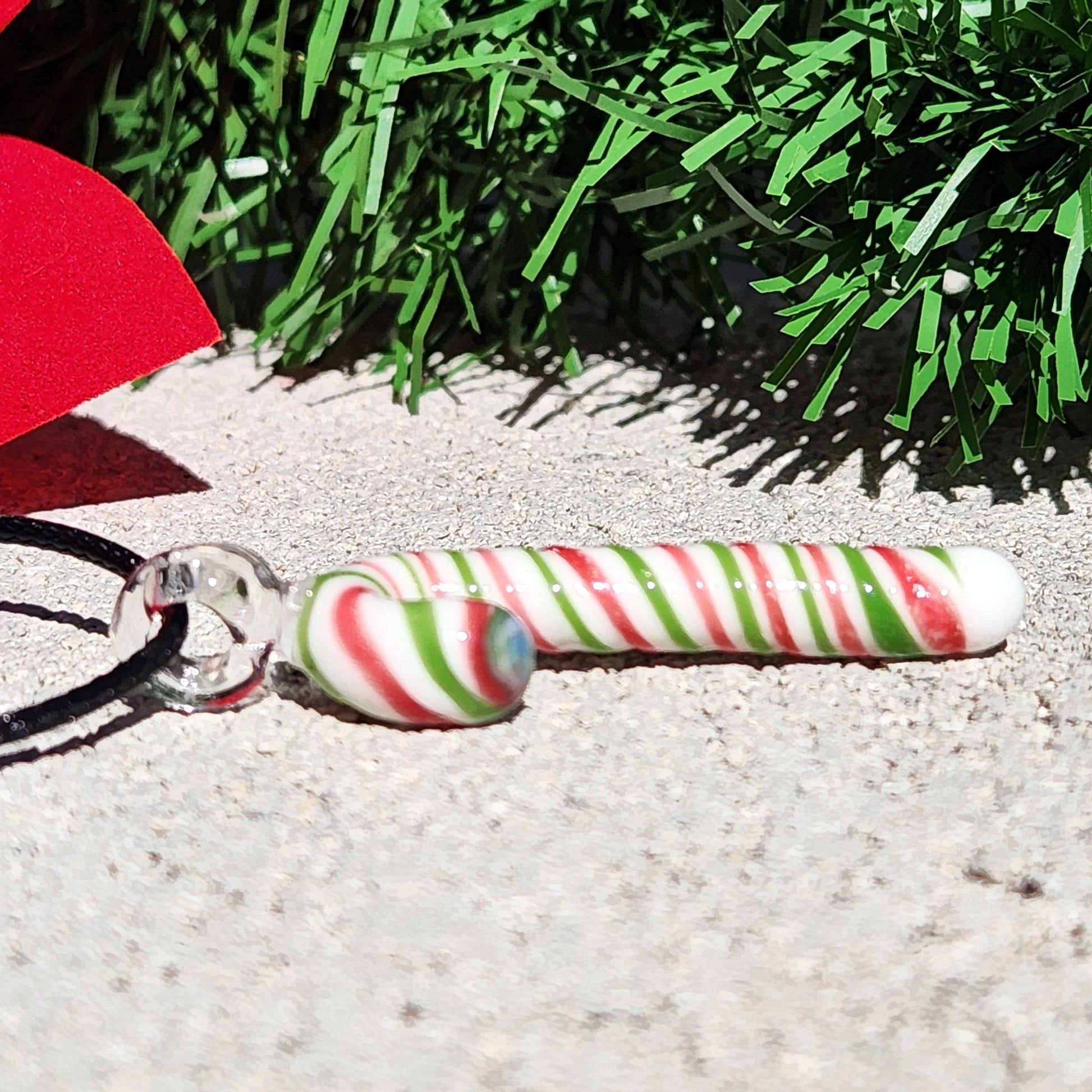 Horizontal view of handmade glass candy cane pendant with red, green, and white stripes, showcasing its glossy finish and festive design.
