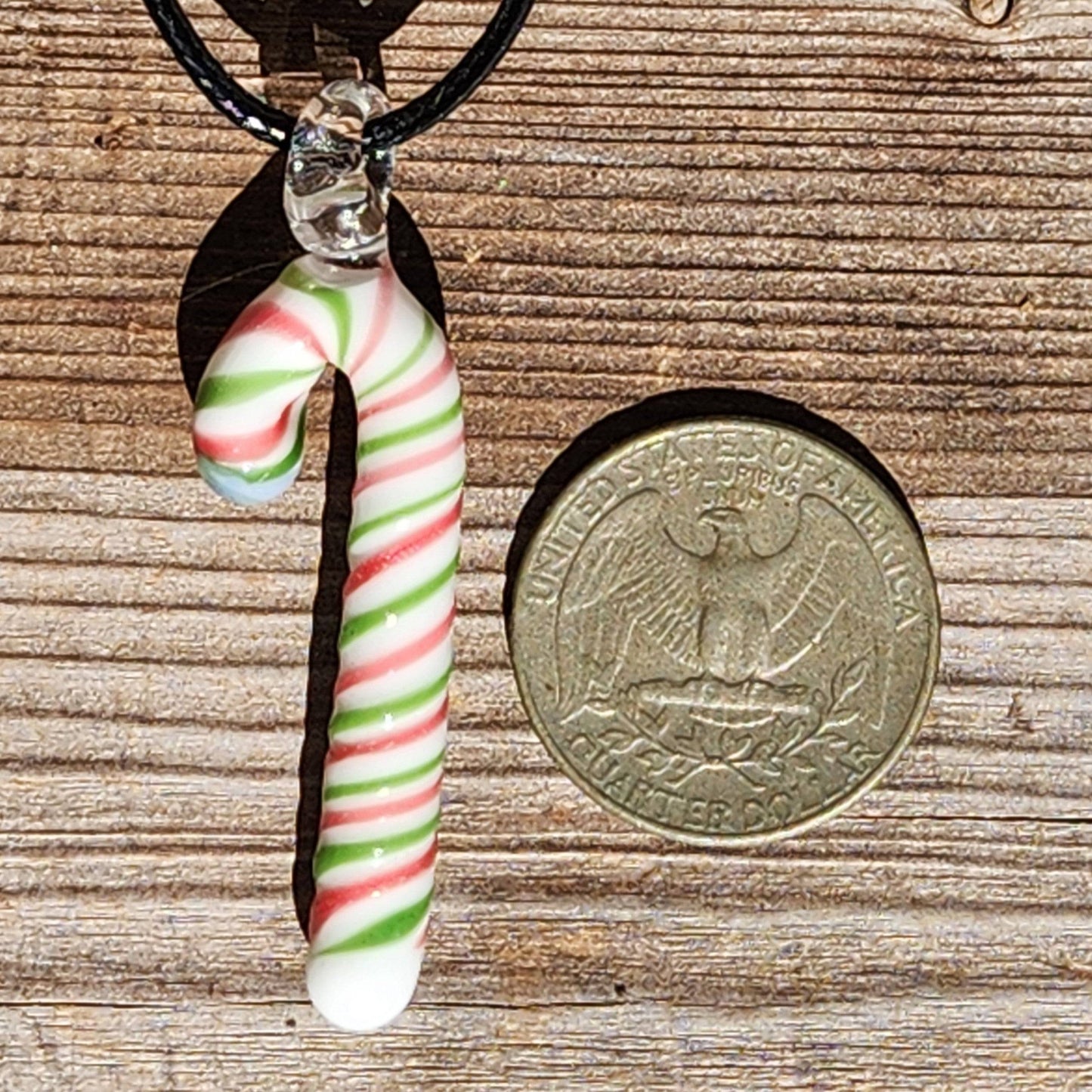 Handmade glass candy cane pendant necklace shown next to a U.S. quarter for size reference, highlighting its compact festive design.