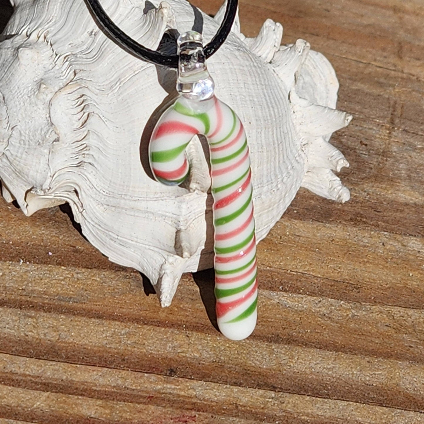 Handmade glass candy cane pendant necklace resting on a wooden surface, highlighting its Christmas-themed red, green, and white swirl pattern.