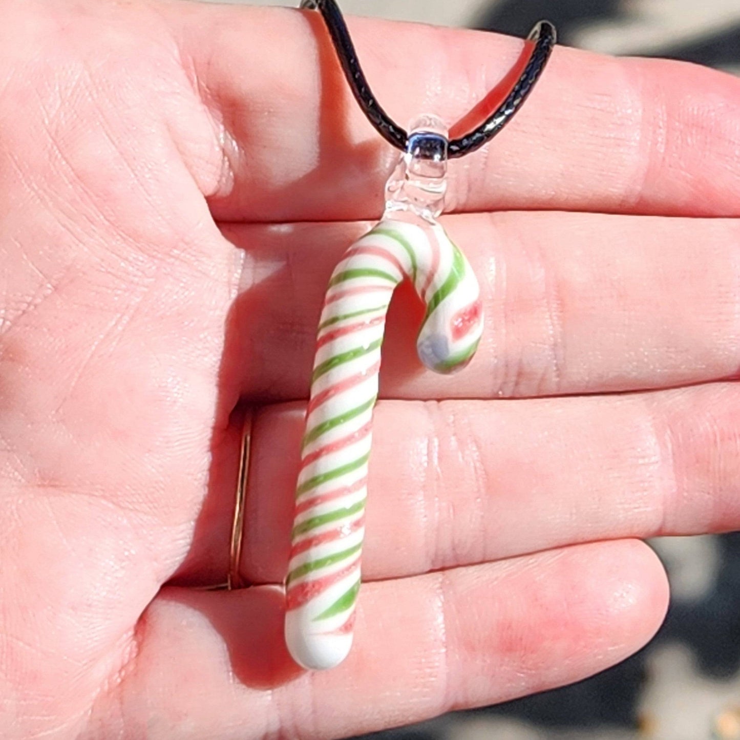 Hand displaying handmade glass candy cane pendant necklace with red, green, and white stripes, perfect for holiday jewelry gifting.