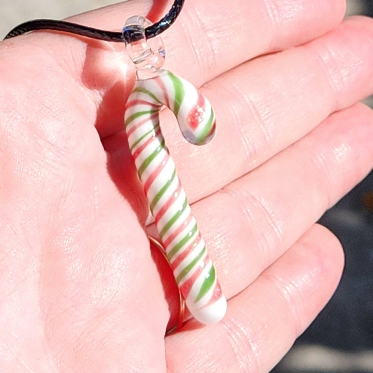 Hand holding handmade glass candy cane pendant necklace, showing its size and colorful Christmas-themed swirl pattern.
