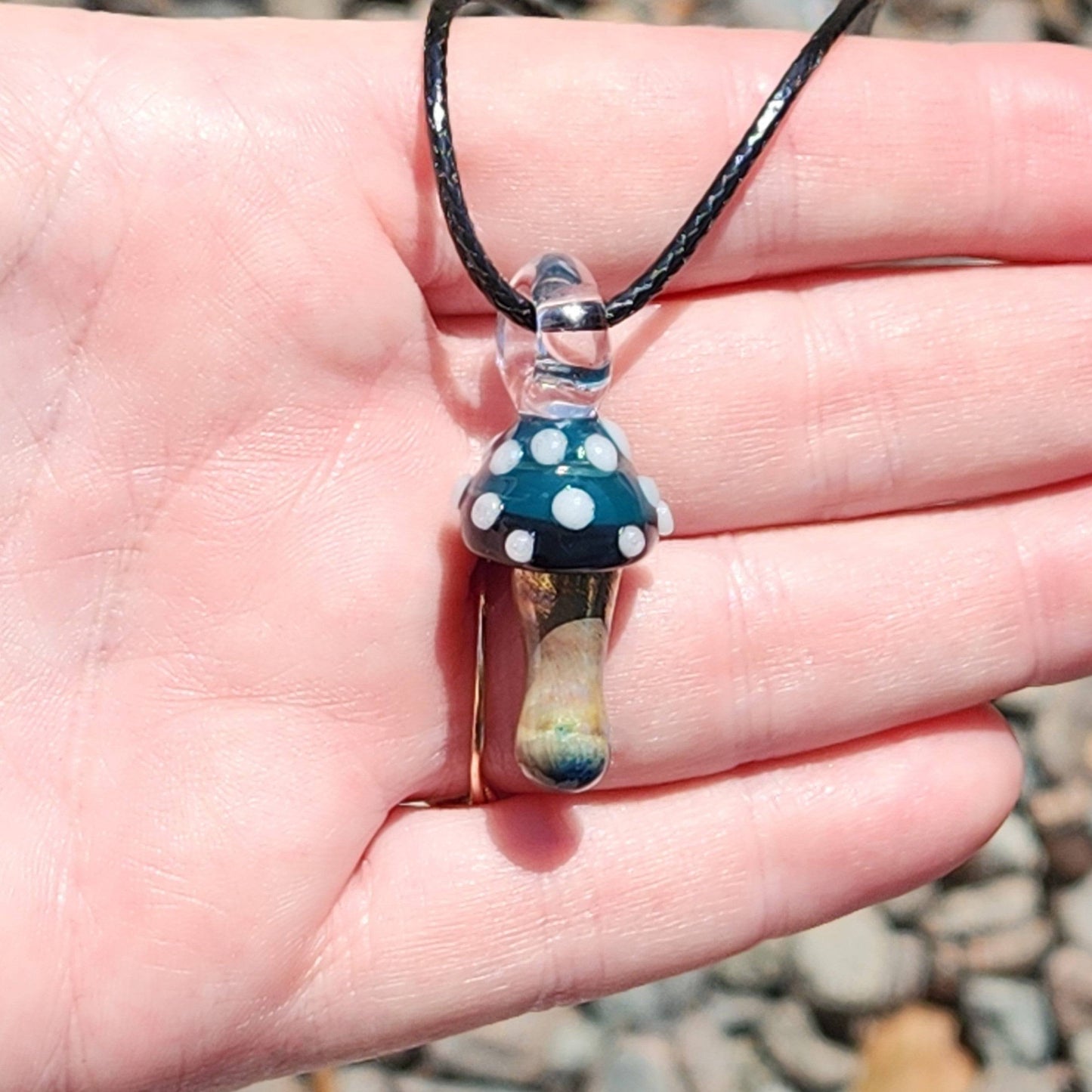Hand holding Blue Mushroom Art Glass Pendant Necklace with metallic stem and blue cap. A unique handmade accessory for nature enthusiasts.