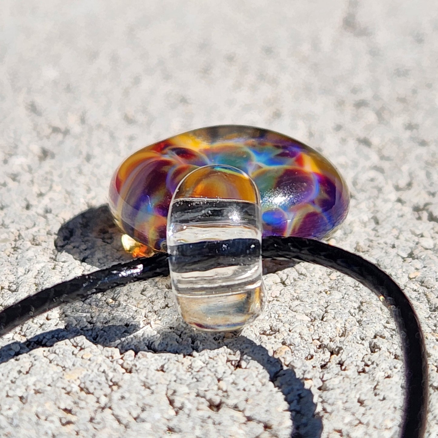 Colorful glass pendant on a black cord, placed on a sandy background