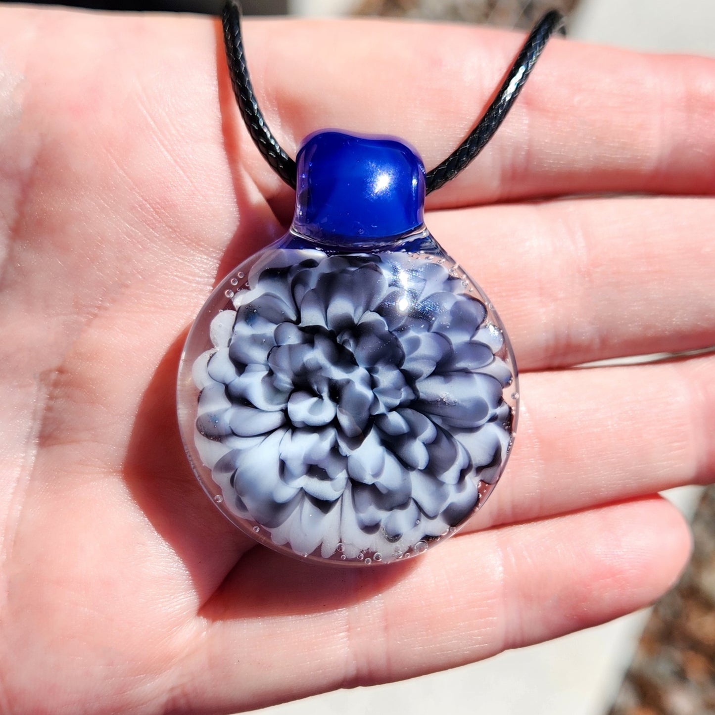 Blue blown glass pendant with floral design on a black cord, detailed view