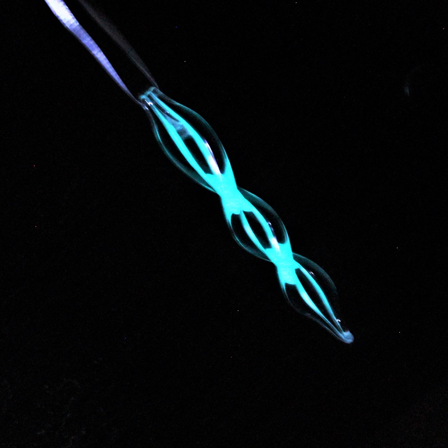 Single glow-in-the-dark glass ornament glowing bright blue in the dark. Unique handmade Christmas keepsake for indoor or outdoor holiday decor.