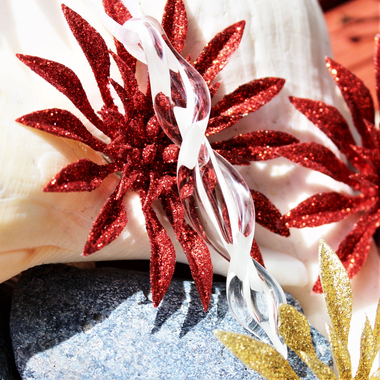 Clear spiral glass ornament displayed with red glitter poinsettias and seashells. Handmade holiday decoration for Christmas or beach-themed decor.