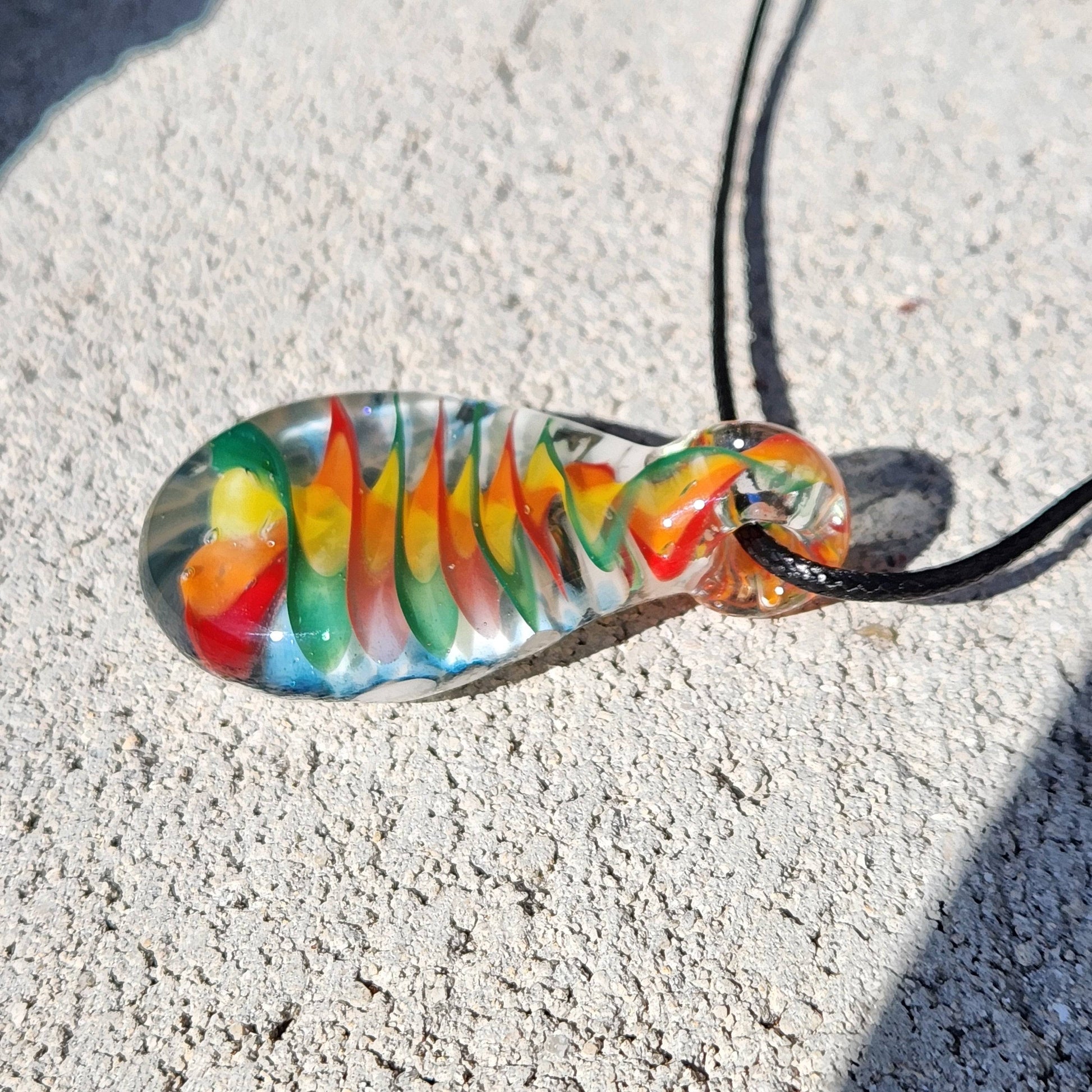 Angled view of handmade glass pendant necklace showcasing the vivid spiral rainbow design and teardrop shape on a stone background.