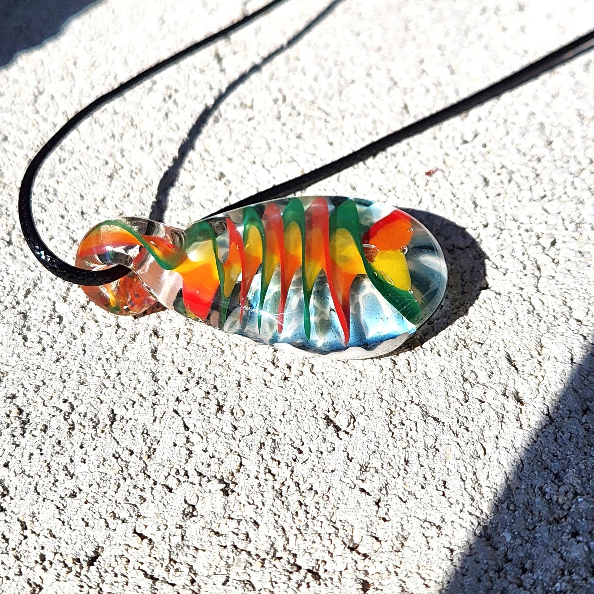 Handmade glass pendant necklace with spiral rainbow design, photographed in sunlight to highlight the vibrant colors and clarity of the glass.