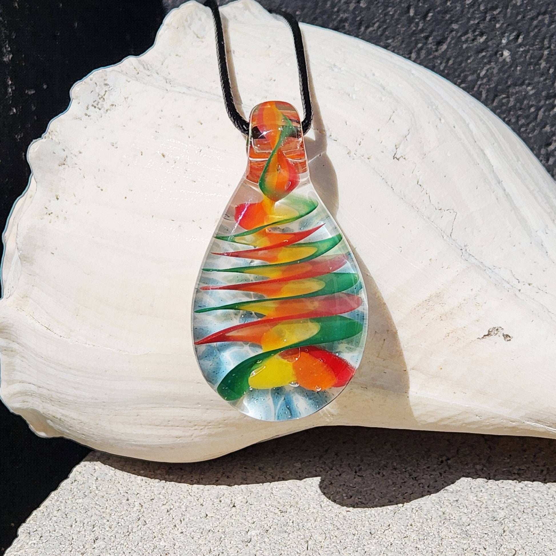 Handmade glass pendant necklace with spiral rainbow design displayed on a white seashell. Vivid colors swirl inside the teardrop-shaped glass.