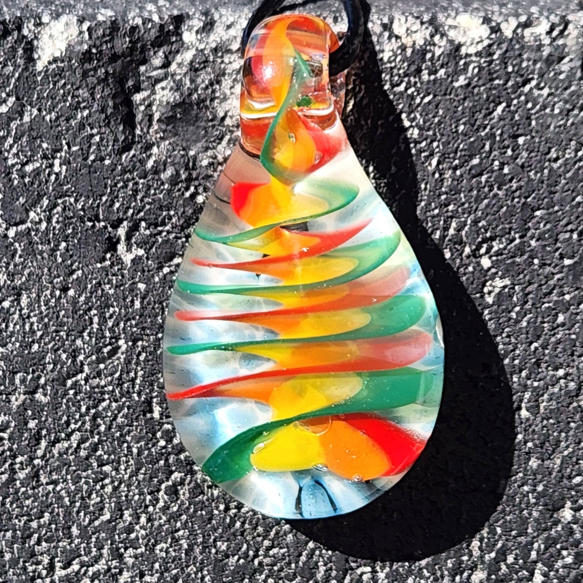 Handmade glass pendant necklace with multicolor spiral design hanging against a dark textured wall, emphasizing the vivid rainbow swirl.