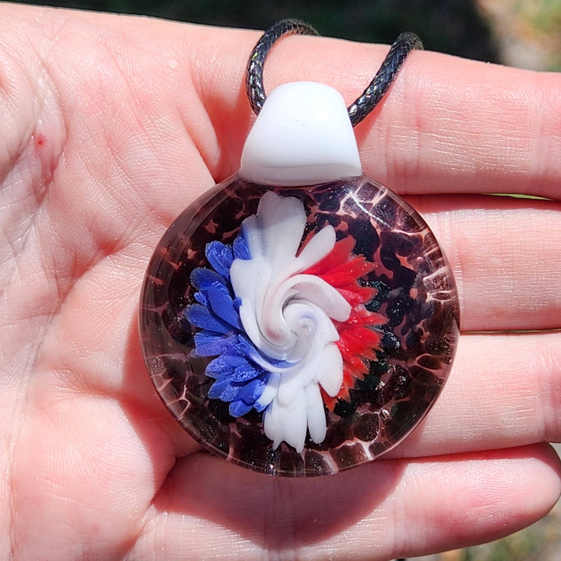Hand holding large handmade glass pendant with red, white, and blue floral swirl. Unique trippy necklace charm for gifts.