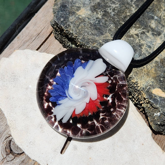 Unique handmade blown glass pendant necklace with red, white, and blue swirl design on black background. Bold trippy flower pattern for jewelry lovers.