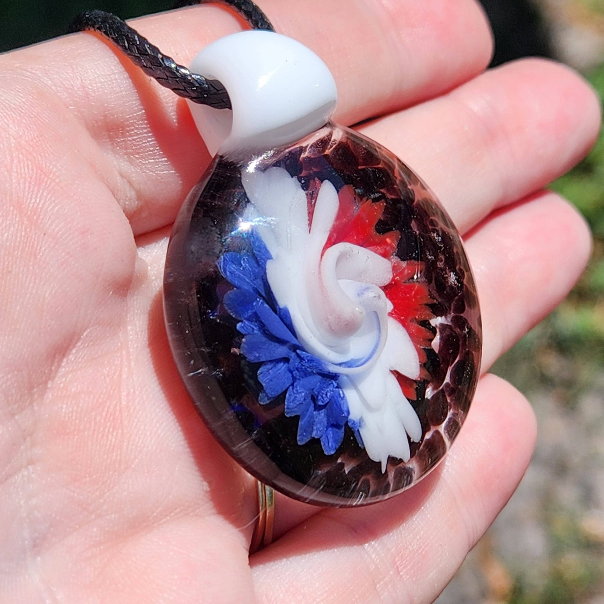Close-up of glass pendant in hand, showcasing red, white, and blue swirl flower. Handmade jewelry for bold accessory lovers.