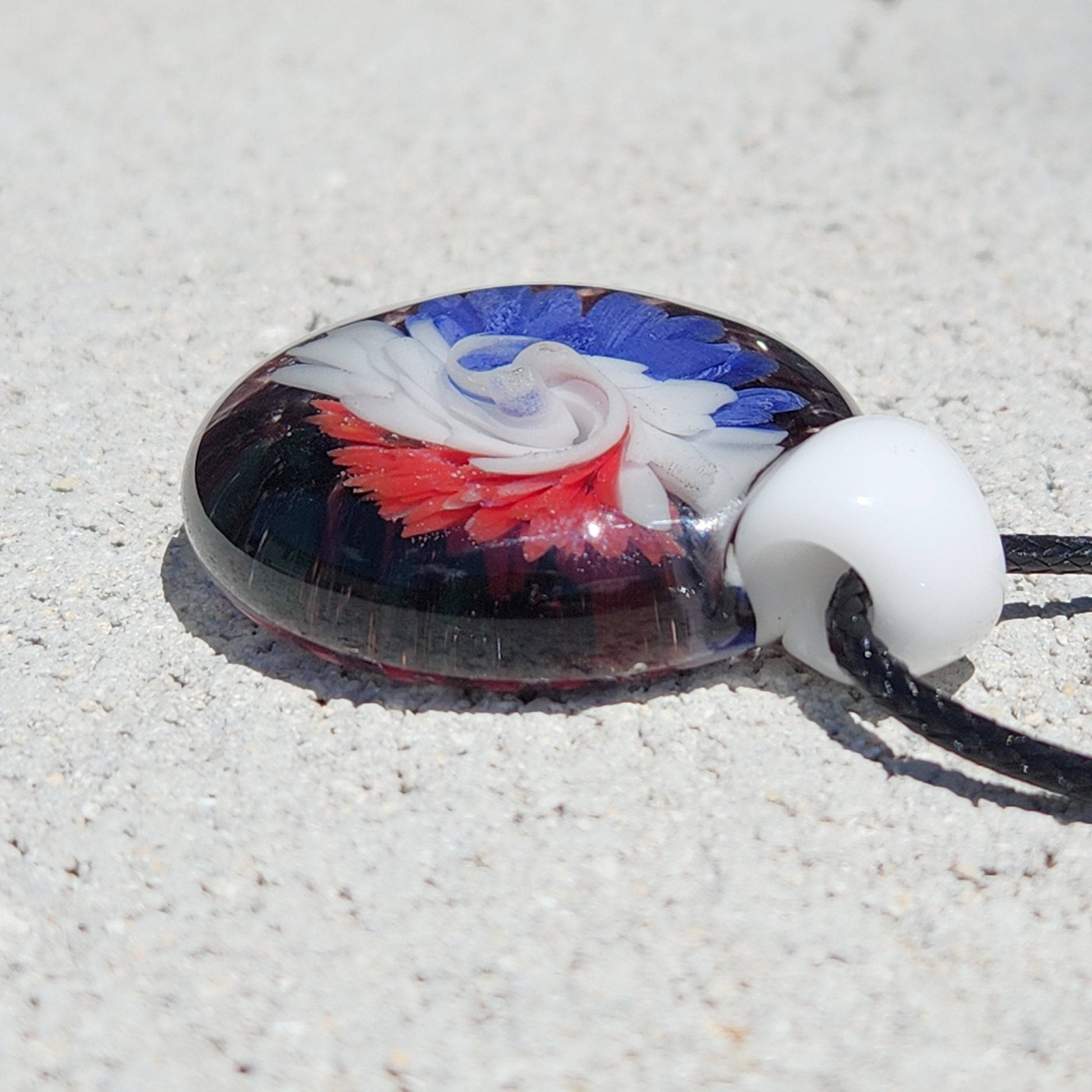 Side view of handmade blown glass pendant with patriotic red, white, and blue swirl design. Unique accessory for pendant necklace collections.