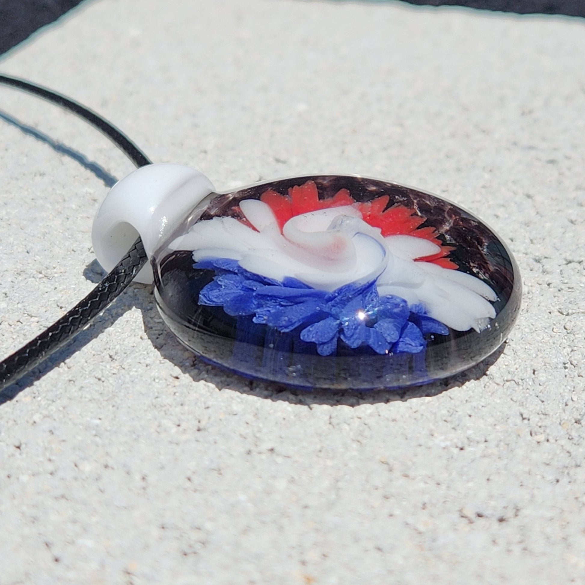 Flat angle of blown glass pendant necklace with red, white, and blue swirl flower. Artistic jewelry piece for bold fashion statements.
