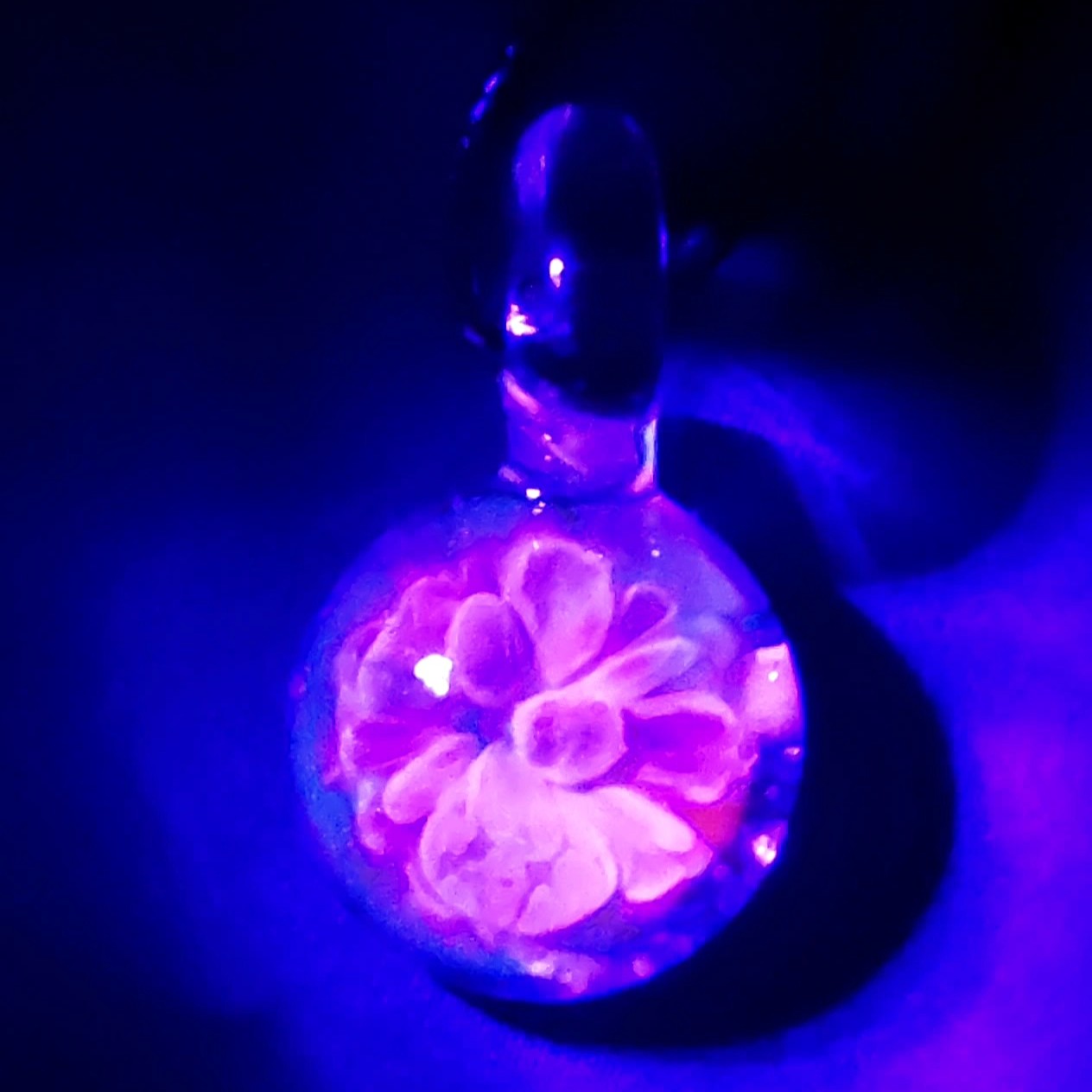 UV glow view of Handmade Borosilicate Glass Pendant showing vibrant pink and purple floral bloom under blacklight.