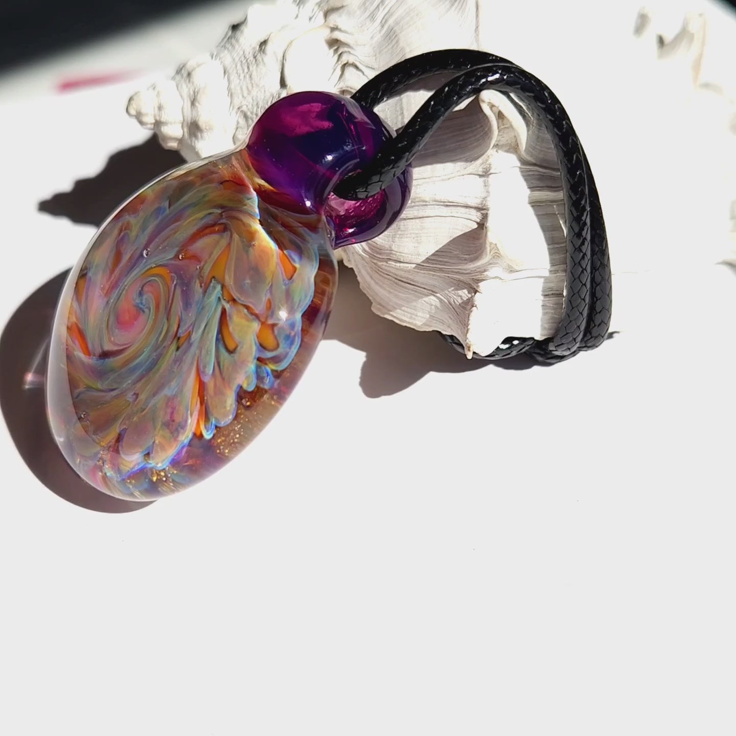 Handmade blown glass pendant featuring a swirling borosilicate design in vibrant purple, orange, and gold tones. Unique jewelry charm for necklaces.
