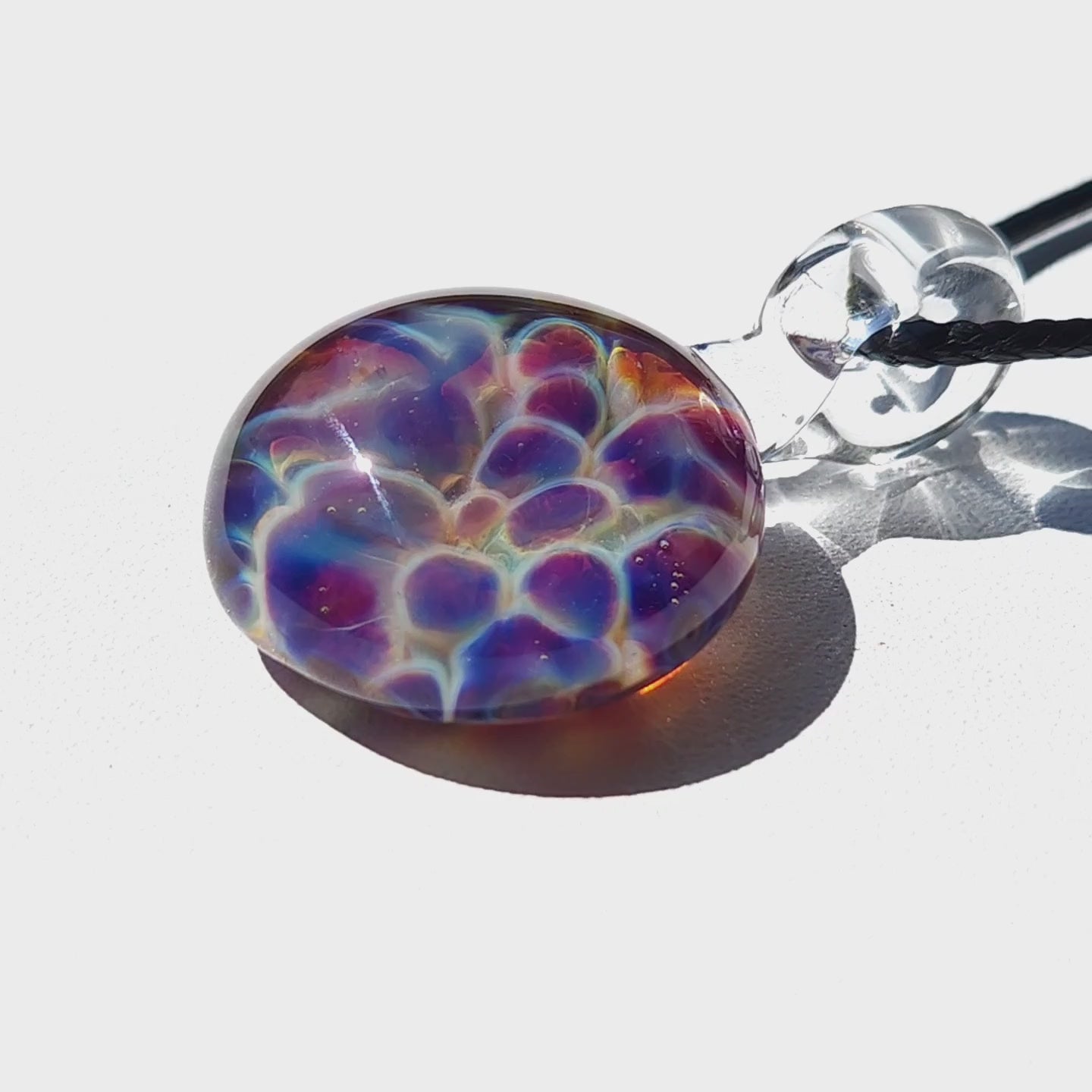 Close-up of handmade glass pendant with iridescent purple and blue bubble design, shown on white background for jewelry detail.