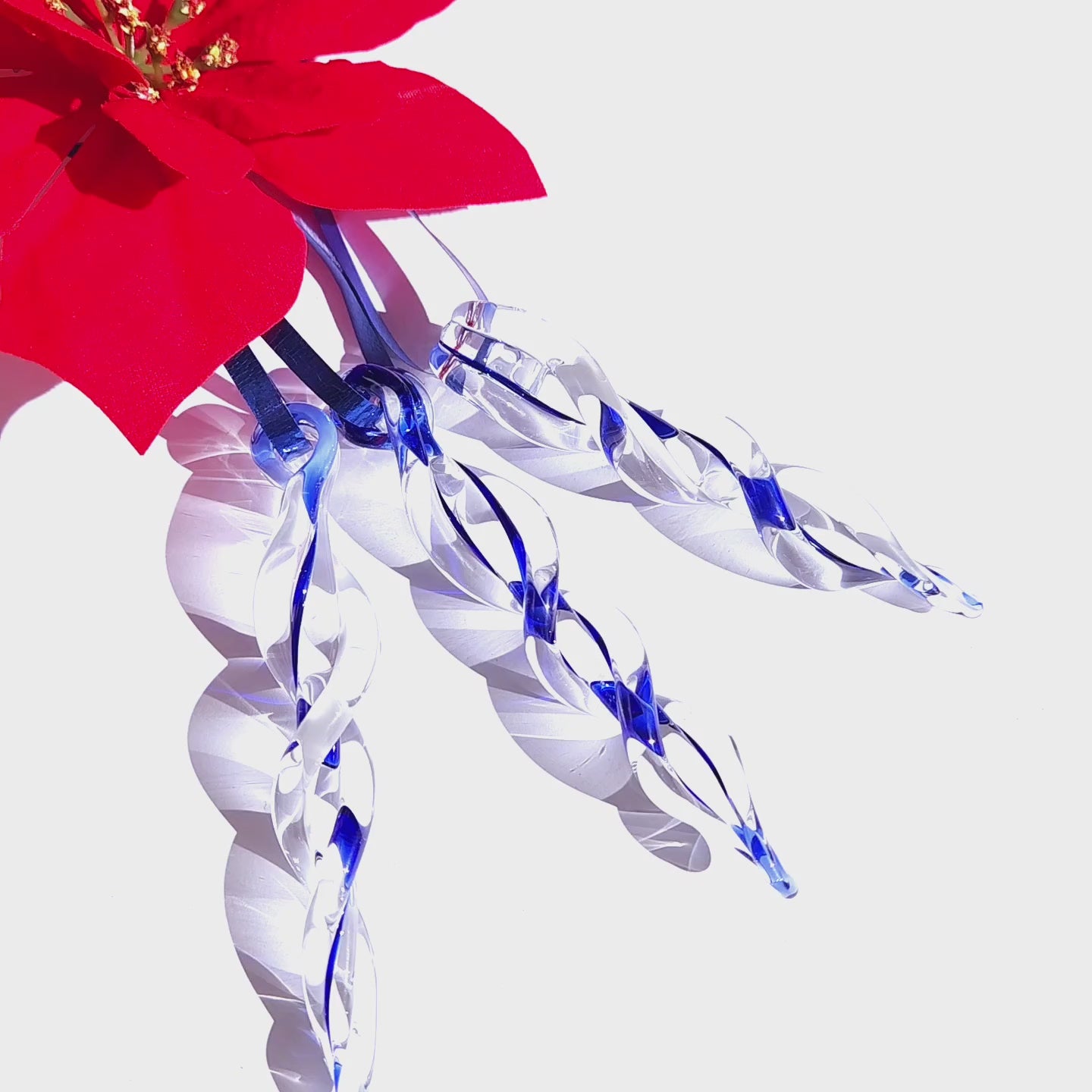 Four handmade blue glass icicle ornaments hanging beneath a red poinsettia, ideal for festive Christmas tree or window decor.