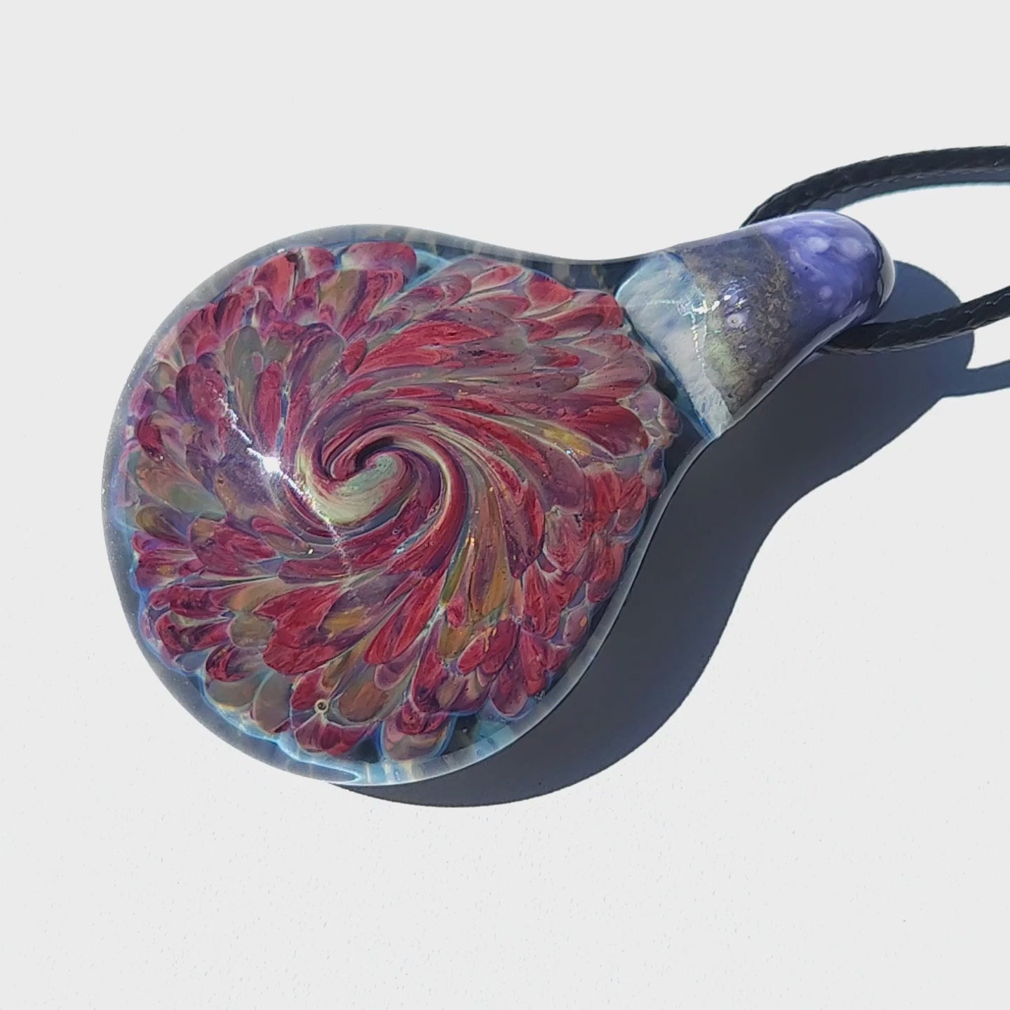 Handblown heady glass pendant necklace with vivid red and amber swirl on white background. Unique handmade jewelry gift in borosilicate glass.