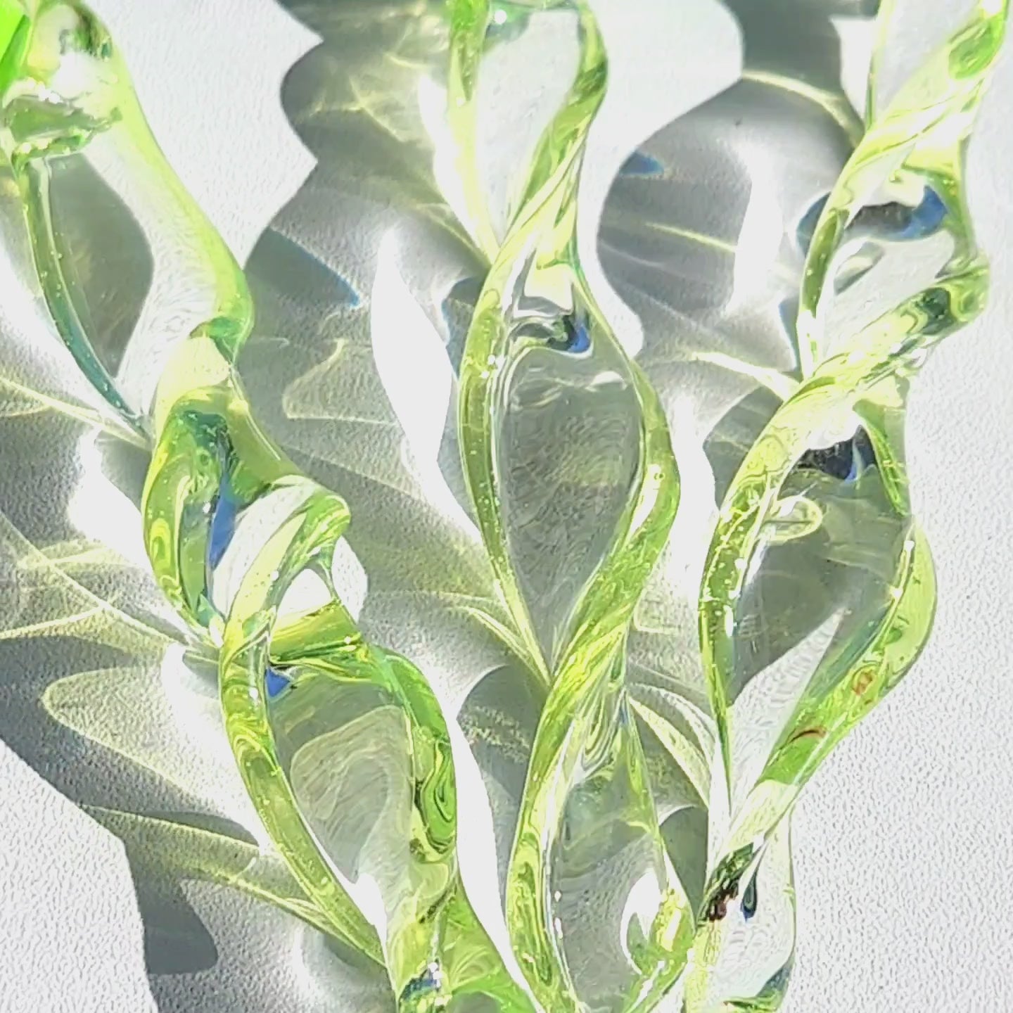 Sunlight shining through lime green spiral glass suncatchers, casting reflections and showcasing their twisted handmade design.