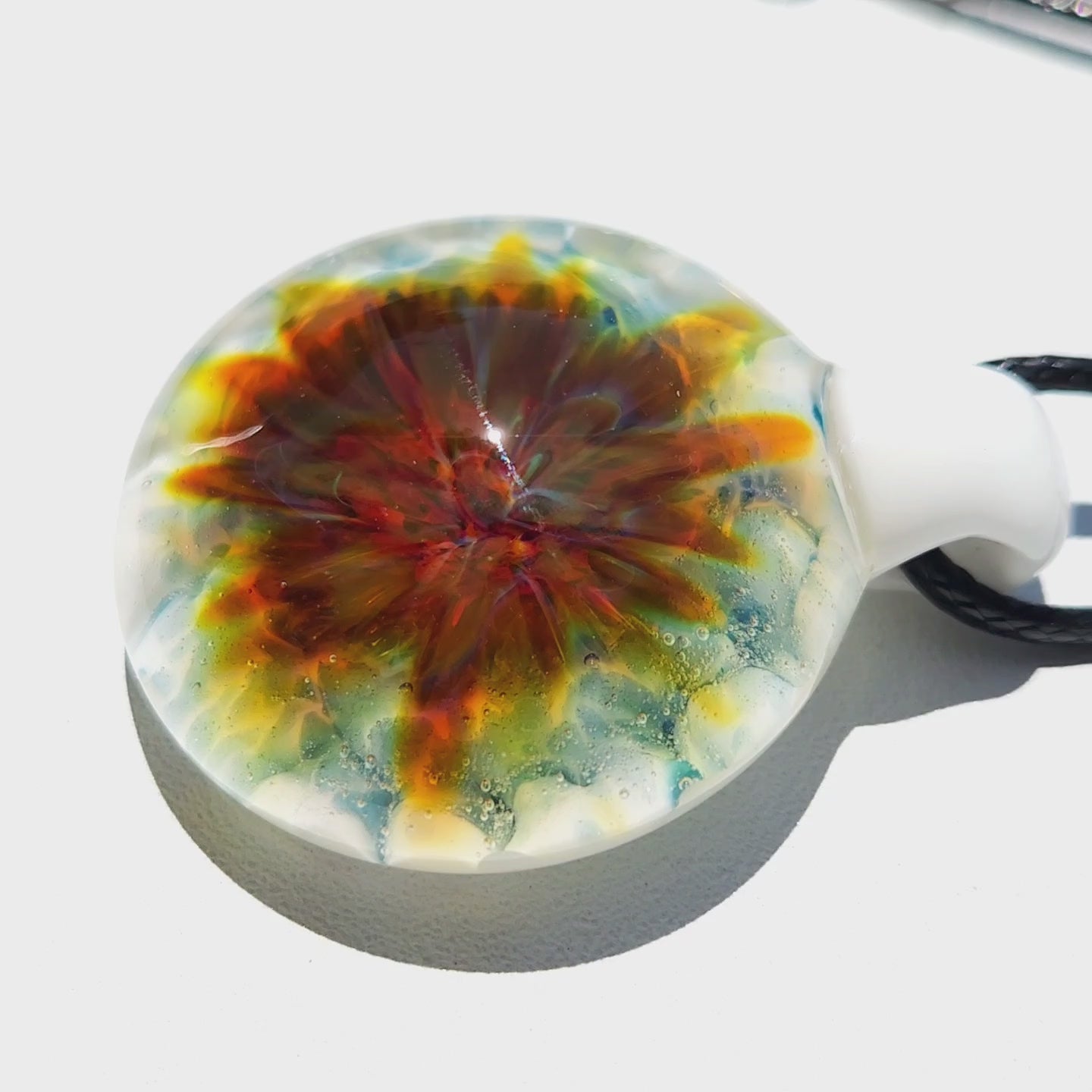 Close-up of handmade glass pendant with radiant flower pattern in warm tones on a white background. Unique lampworked glass jewelry piece.