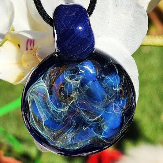 Handmade heady glass pendant necklace with swirling blue, silver, and gold fumed design on dark blue glass, perfect for unique jewelry lovers.