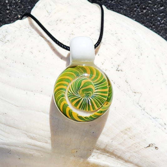 Handmade Spiral Glass Pendant with green and yellow swirl on white background, displayed on a shell. Unique blown glass jewelry gift.