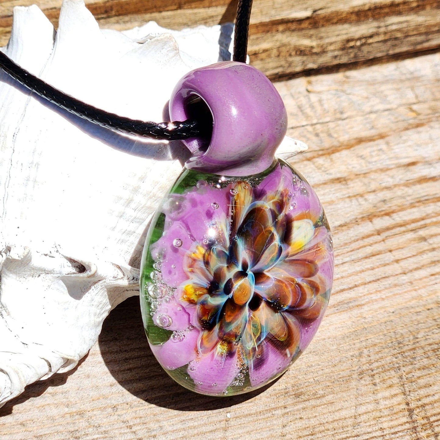 Close-up of handmade borosilicate pendant with multicolor flower and purple loop. Artistic glass jewelry for fashion accessories.