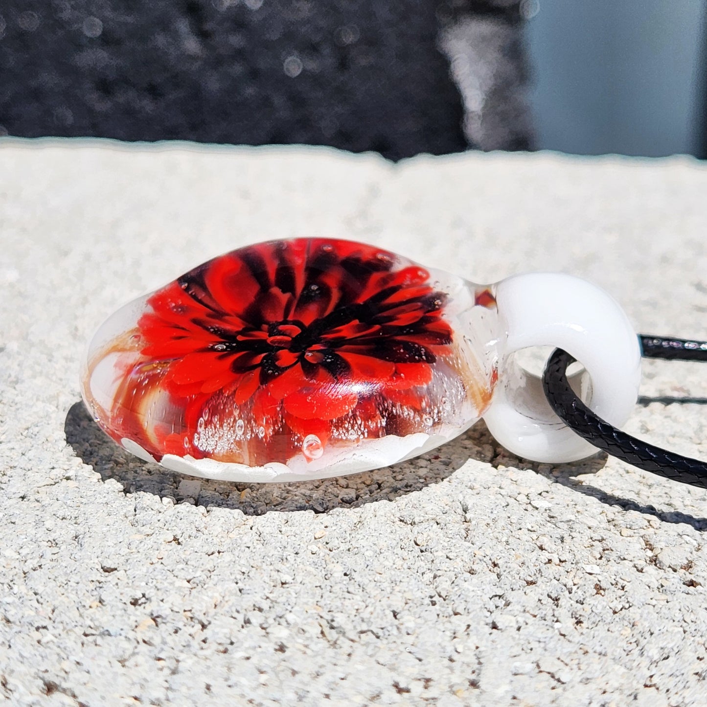 Side view of Red Flower Glass Pendant Necklace on stone, highlighting the domed glass and vivid floral detail.