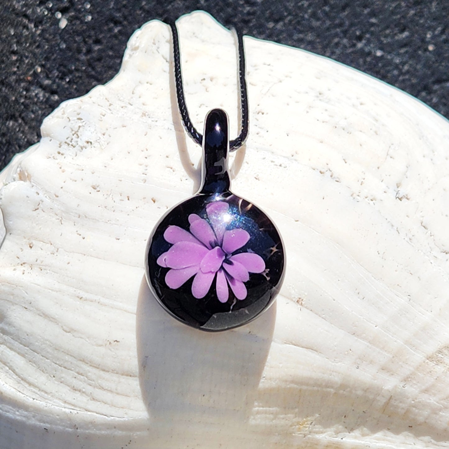 Minimalist purple glass pendant with black background, handmade in the USA, displayed on a white seashell for jewelry product showcase.