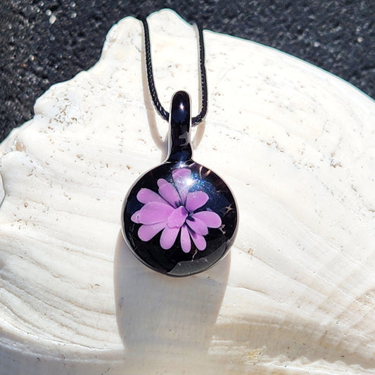Minimalist purple glass pendant with black background, handmade in the USA, displayed on a white seashell for jewelry product showcase.