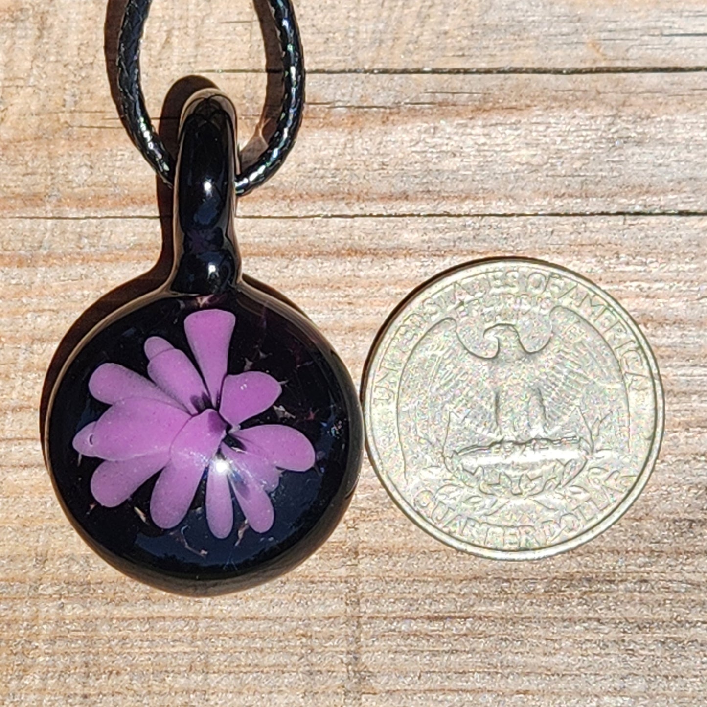 Size comparison of handmade purple flower glass pendant next to US quarter, highlighting compact design of minimalist statement necklace.