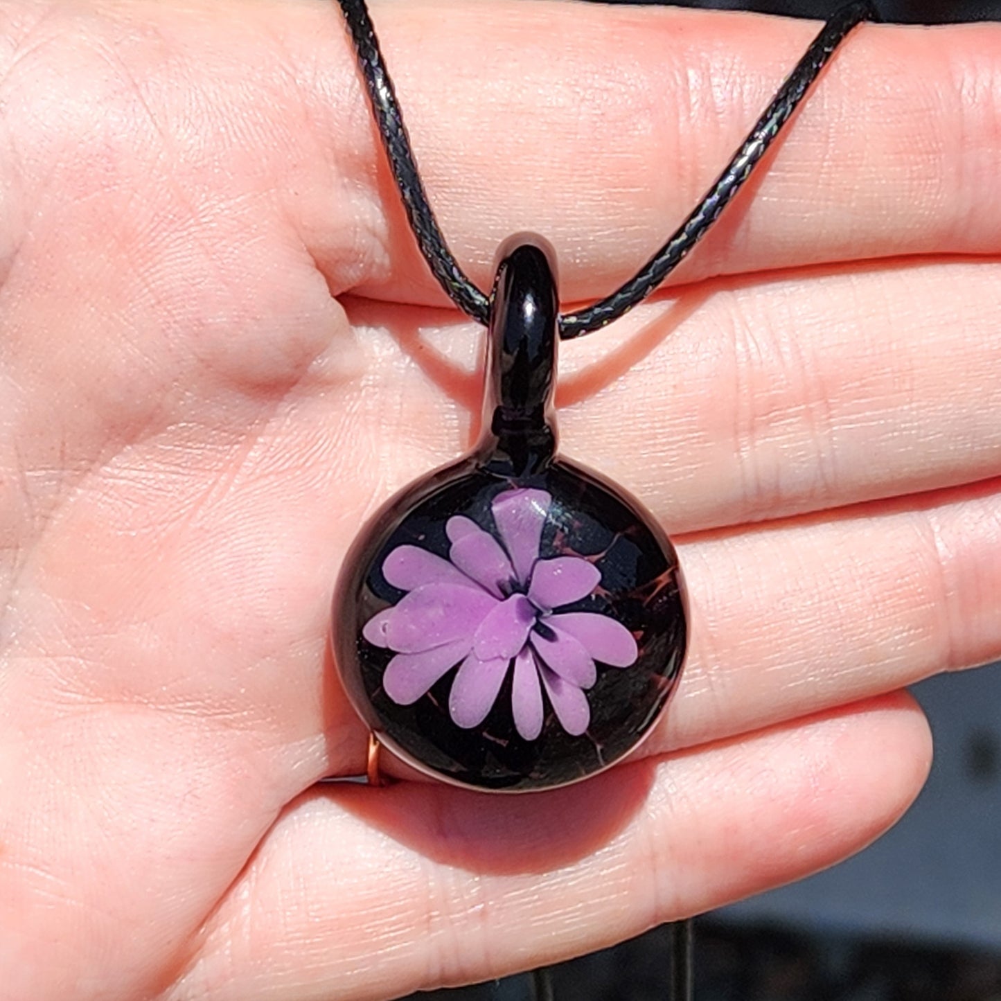 Hand holding a small handmade purple flower glass pendant necklace, showcasing size and detail of minimalist jewelry piece.
